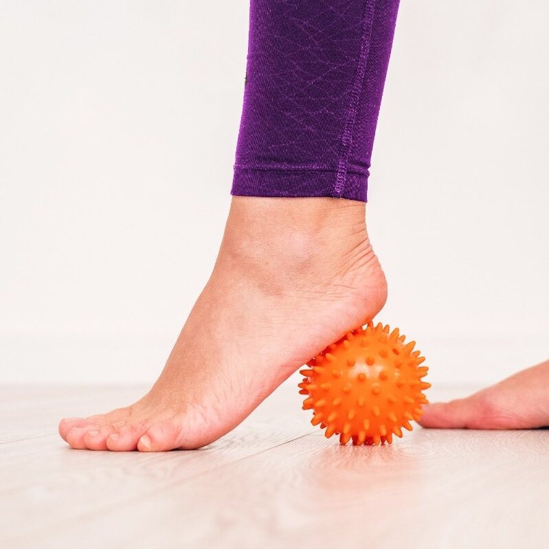 un piede scalzo col tallone appoggiato su una pallina di gomma con piccole protuberanze usata per automassaggio